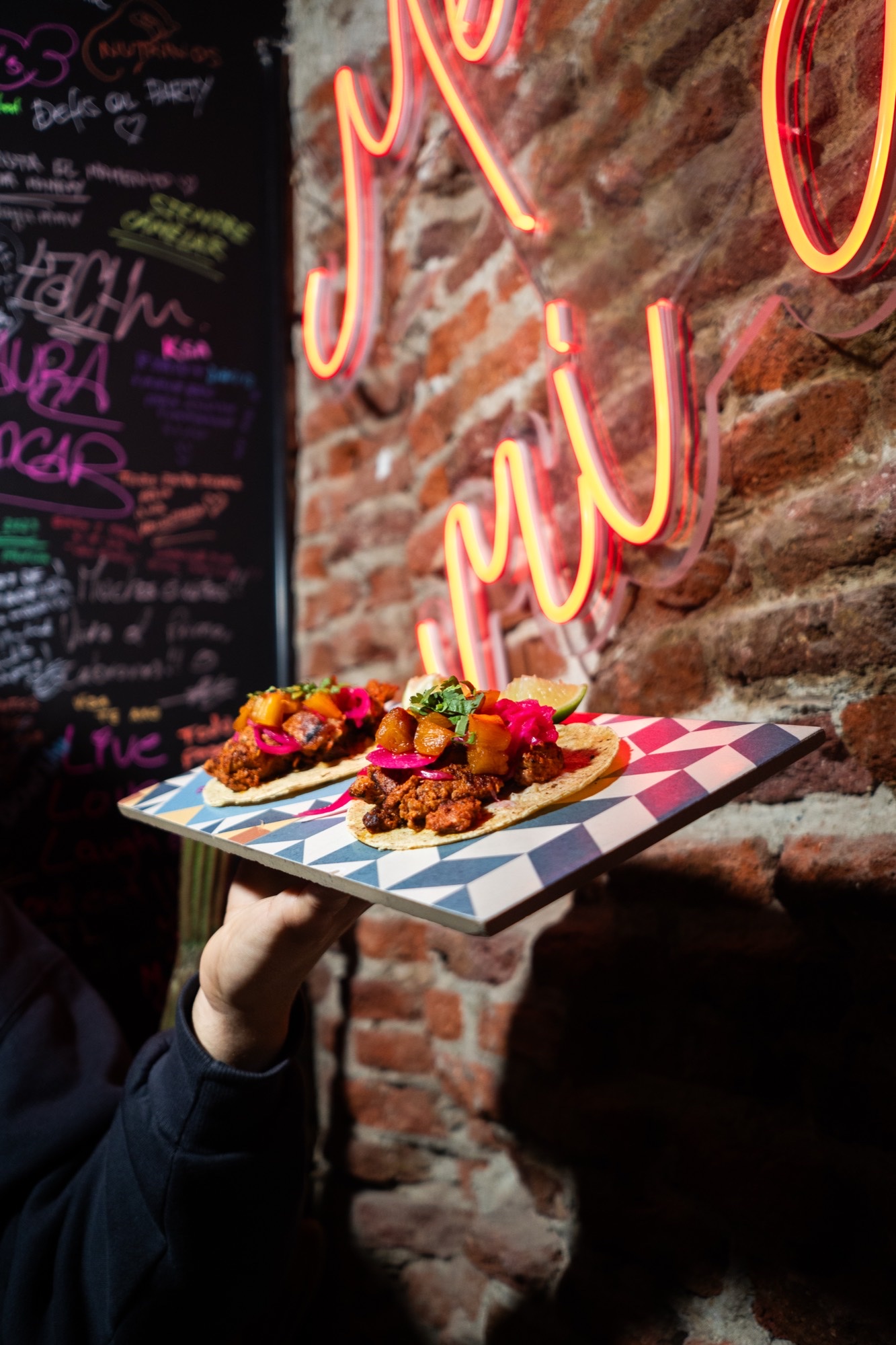 Tacos al pastor de Primo con piña asada y cebolla roja encurtida, servidos bajo el neón del local en el centro de Madrid